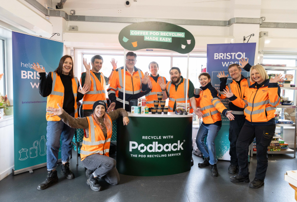 10 staff in hi-vis jackets standing around a coffee pod collection bin