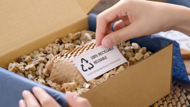hand holding label saying 100% recyclable in cardboard box with recyclable packing material